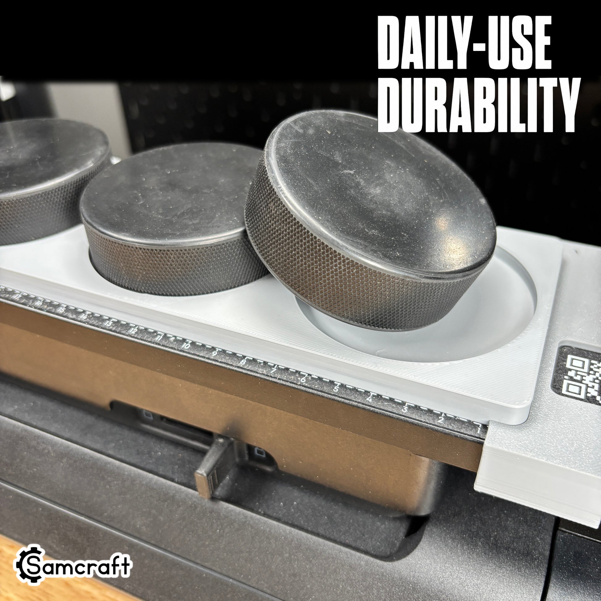 Hockey Puck Jig for the eufyMake E1 — close-up of black hockey pucks resting in the round pockets of the gray one-piece tray with built-in alignment ruler and QR code, built for daily-use durability.