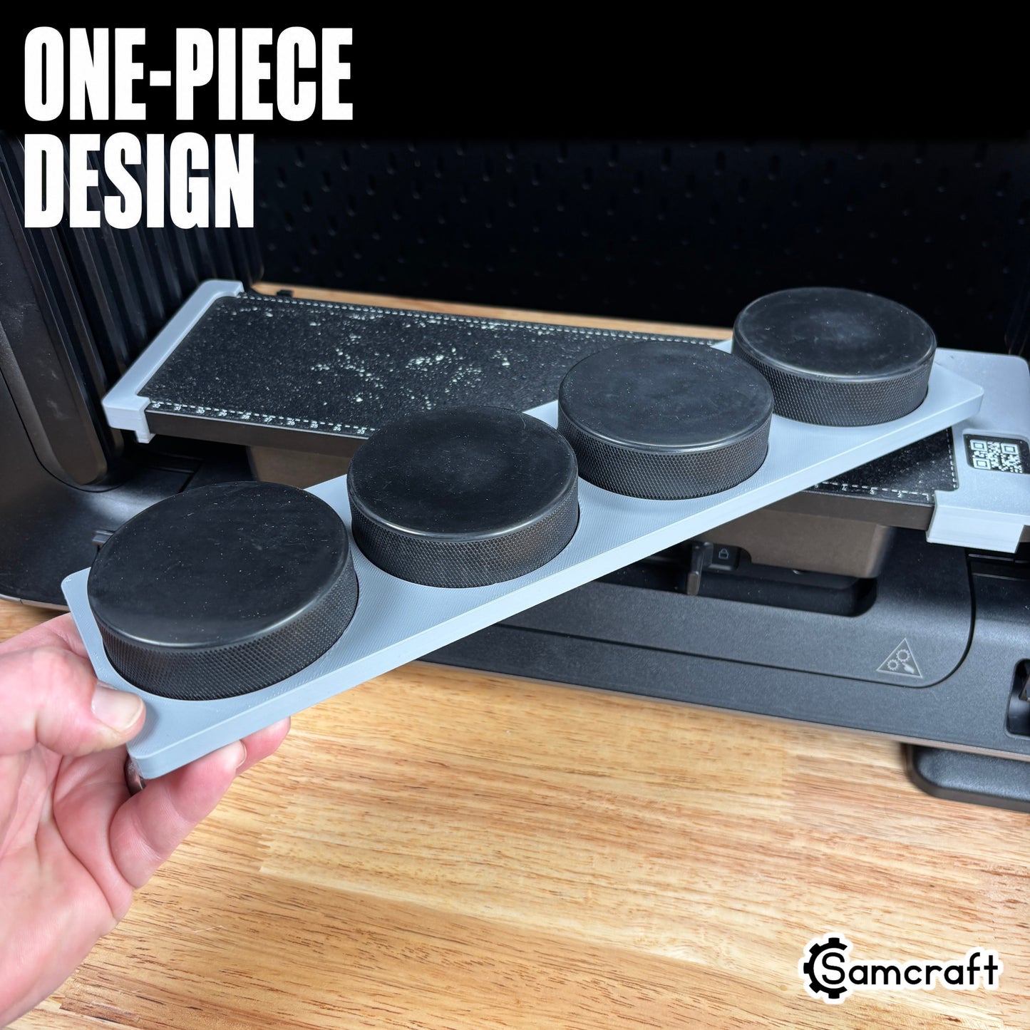Hockey Puck Jig for the eufyMake E1 — hand holding the gray one-piece 3D-printed tray loaded with four black hockey pucks in their round molded pockets, with the built-in measurement ruler, showing the solid single-piece design.