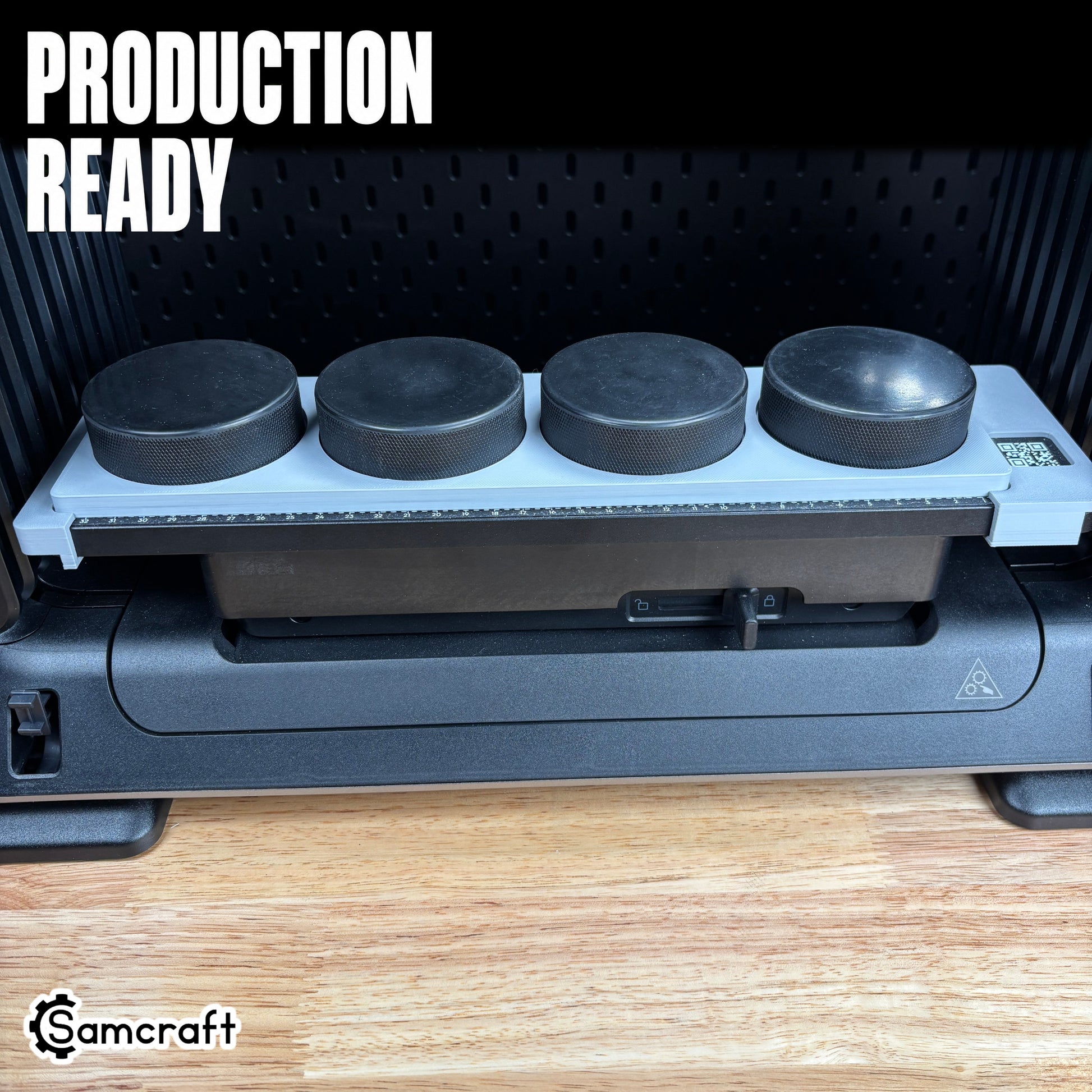 Hockey Puck Jig for the eufyMake E1 — four black hockey pucks lined up in the gray one-piece tray mounted on the printer bed, alignment ruler and QR code along the edge, set up for production-ready batch printing.