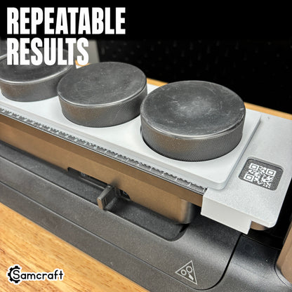 Hockey Puck Jig for the eufyMake E1 — angled view of black hockey pucks held in the round pockets of the gray 3D-printed tray with built-in alignment ruler and QR code, positioned for repeatable, consistent print results.