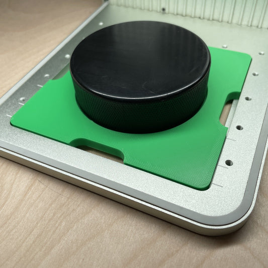 Samcraft green hockey puck jig in an xTool F1 laser bed, cradling a regulation black hockey puck.