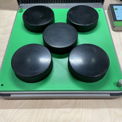 Samcraft green hockey puck jig in an xTool F1 Ultra laser bed, holding five regulation black hockey pucks.
