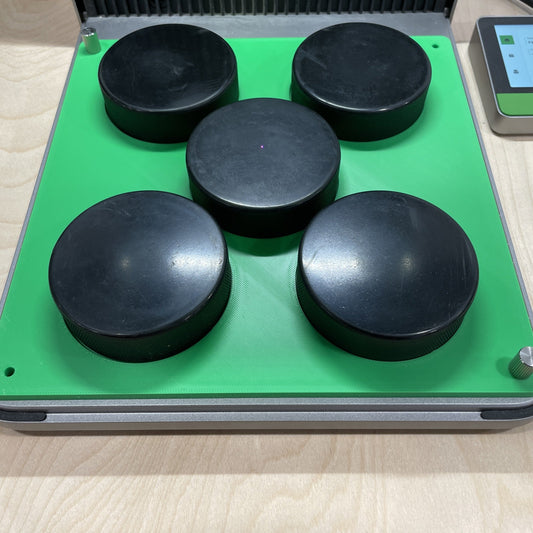 Samcraft green hockey puck jig in an xTool F1 Ultra laser bed, holding five regulation black hockey pucks.