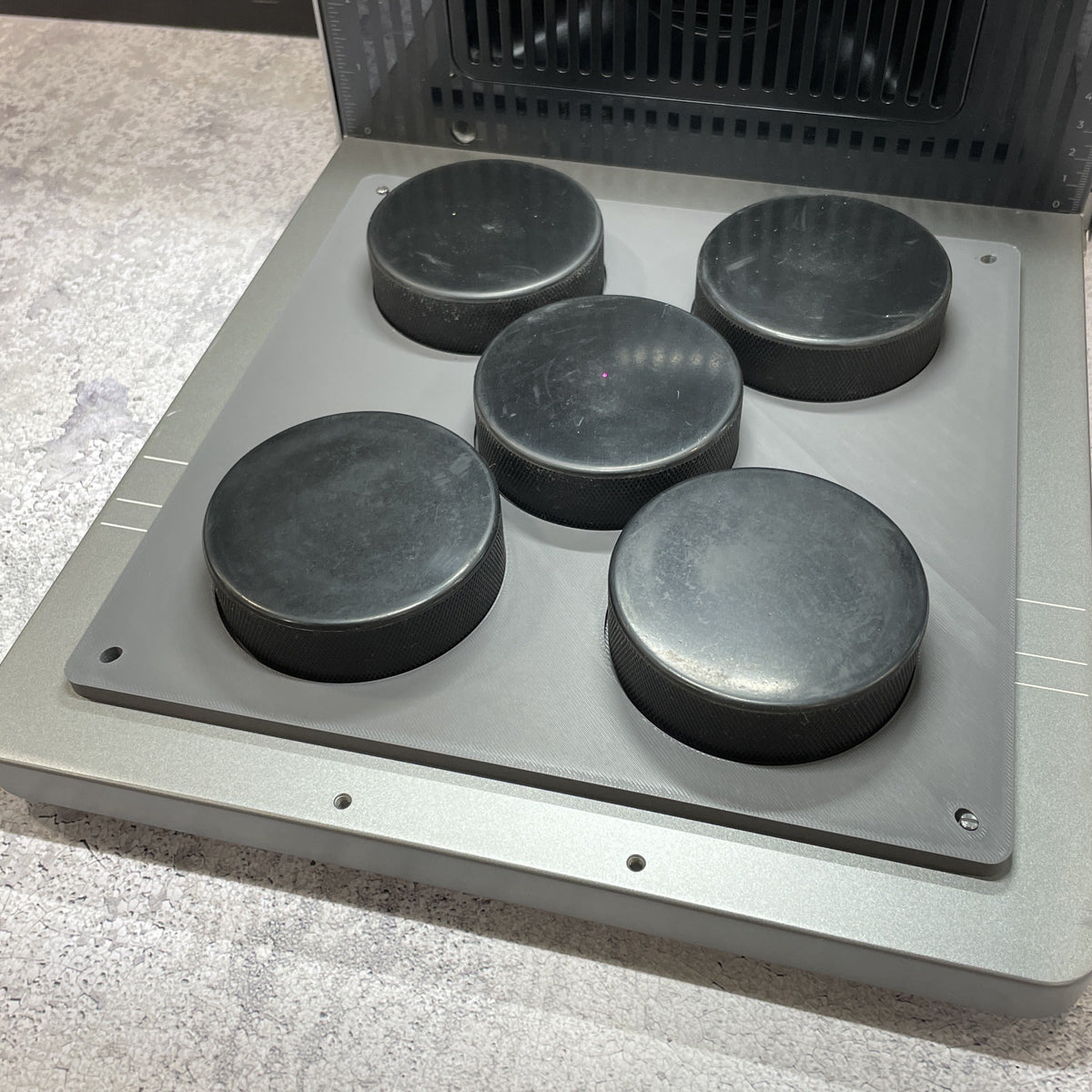 Samcraft hockey puck jig on the xTool F2 Ultra bed, holding five regulation black hockey pucks.