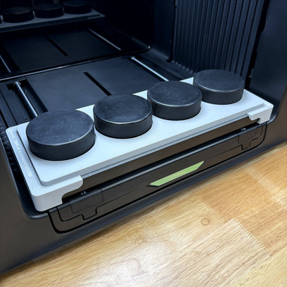 Samcraft hockey puck jig on the bed of an xTool Omni UV printer, holding four black regulation pucks in a single row, seated on the Omni Jig Alignment System.