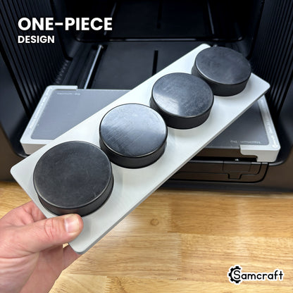 Hand holding the one-piece Samcraft hockey puck jig for the xTool Omni, four black pucks seated in a single molded gray tray.