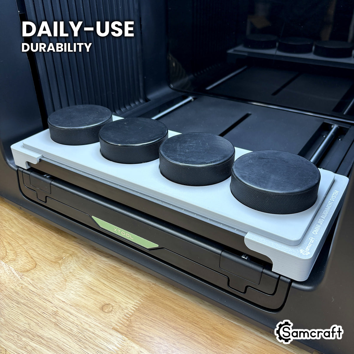 Samcraft hockey puck jig in high-temperature rated plastic holding four black pucks on the xTool Omni bed, built for daily-use durability.