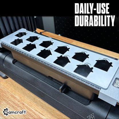 Angled view of the Samcraft House Tag Keychain Jig loaded with black house-shaped keychain blanks in a durable gray tray on the eufyMake E1 UV printer bed.