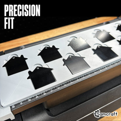 Detail of black and silver house-shaped keychain tags seated in the Samcraft jig's precision-fit pockets, showing tight tolerance and built-in ruler on the eufyMake E1.