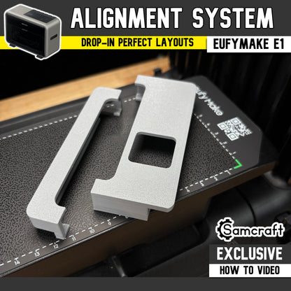 Jig Alignment System for the eufyMake E1 UV printer — two gray 3D-printed alignment guides, an edge rail and a corner bracket with a square cutout, set on the printer's black textured bed for drop-in perfect jig layouts; an original Samcraft design with an exclusive how-to video.