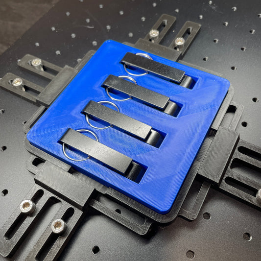 Samcraft blue keychain bottle opener jig on a ComMarker laser bed, holding three steel keychain bottle openers.