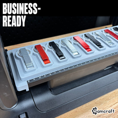 Keychain Bottle Opener Jig for the eufyMake E1 — angled view of silver, red, and black metal keychain bottle openers with split rings seated in the gray 3D-printed tray with built-in alignment ruler, ready for business-scale personalization.