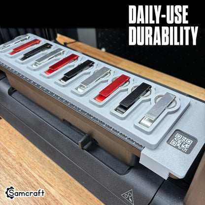 Keychain Bottle Opener Jig for the eufyMake E1 — metal keychain bottle openers in silver, red, and black finishes resting in the shaped pockets of the gray one-piece tray with built-in alignment ruler and QR code, built for daily-use durability.