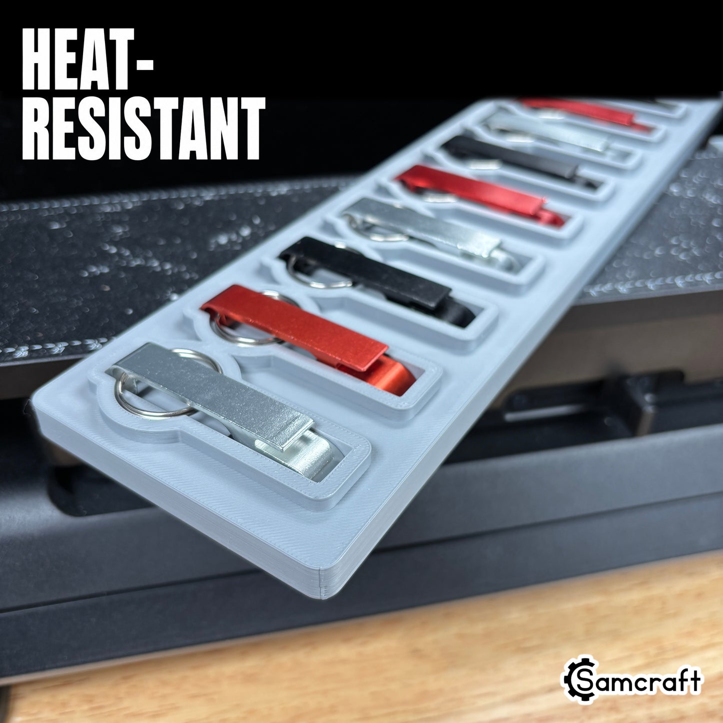 Keychain Bottle Opener Jig for the eufyMake E1 — close-up of silver, red, and black metal keychain bottle openers in the shaped pockets of the gray 3D-printed tray, highlighting the heat-resistant material.