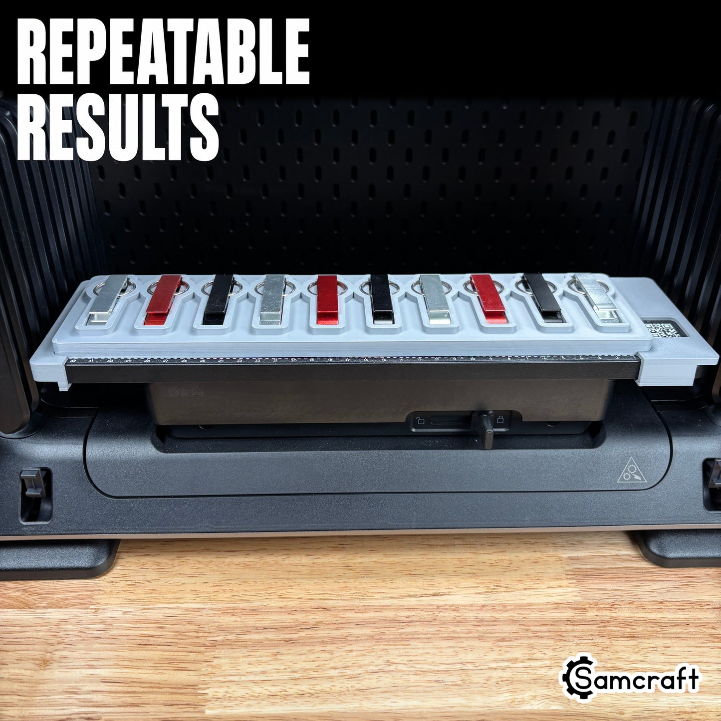 Keychain Bottle Opener Jig for the eufyMake E1 — metal keychain bottle openers in alternating silver, red, and black finishes held in the gray 3D-printed tray with built-in alignment ruler and QR code, positioned for repeatable, consistent print results.