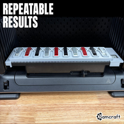 Keychain Bottle Opener Jig for the eufyMake E1 — metal keychain bottle openers in alternating silver, red, and black finishes held in the gray 3D-printed tray with built-in alignment ruler and QR code, positioned for repeatable, consistent print results.
