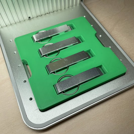 Samcraft keychain bottle opener jig in an xTool F1 laser bed, holding four flat metal keychain bottle openers in a row.
