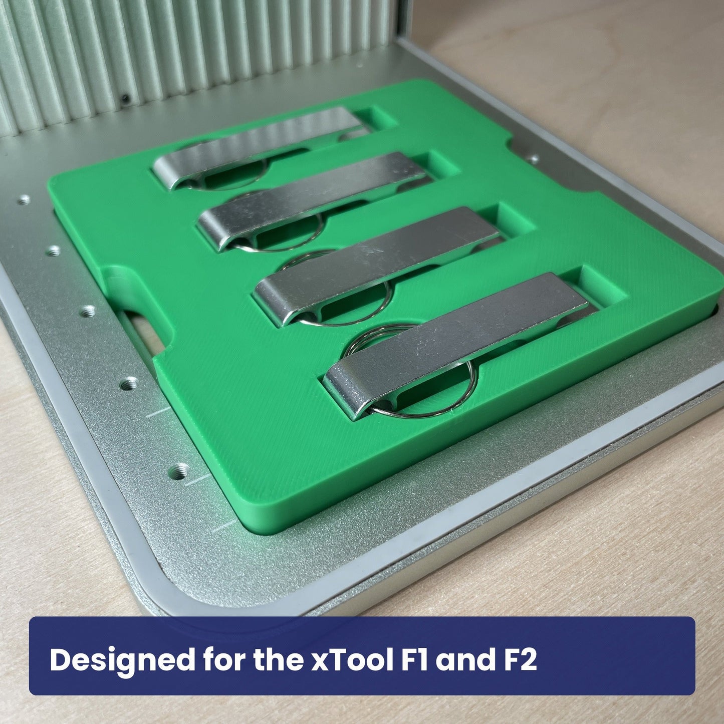 Green Samcraft keychain bottle opener jig seated in the xTool F1 base plate with four metal openers in place.