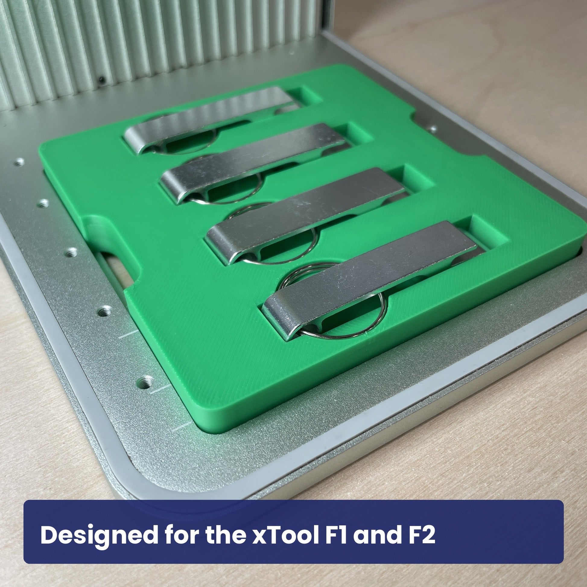 Green Samcraft keychain bottle opener jig seated in the xTool F1 base plate with four metal openers in place.