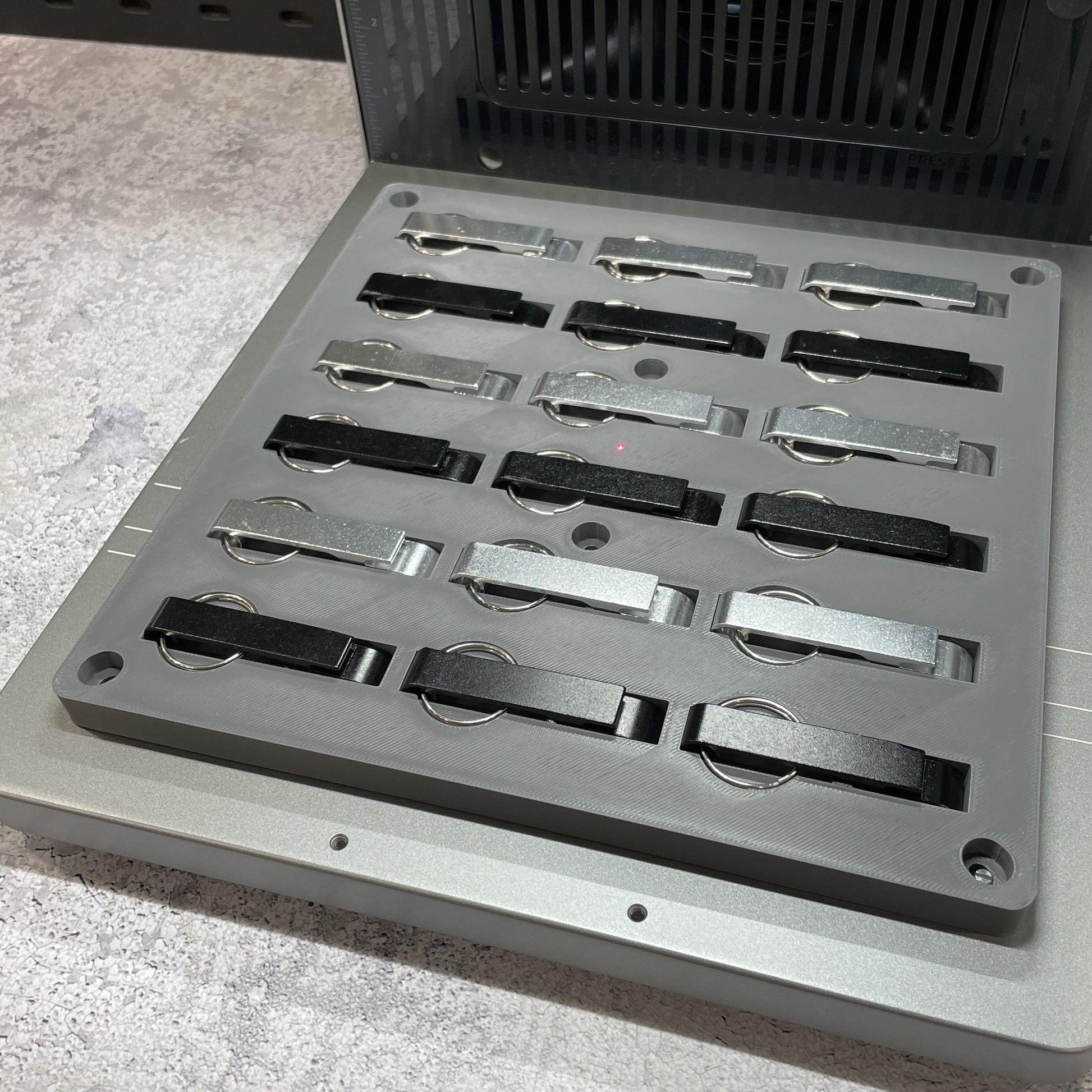 Samcraft keychain bottle opener jig on the xTool F2 Ultra bed, holding rows of metal keychain bottle openers.