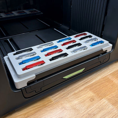 Samcraft keychain bottle opener jig on the bed of an xTool Omni UV printer, holding sixteen aluminum openers in red, blue, black and silver.