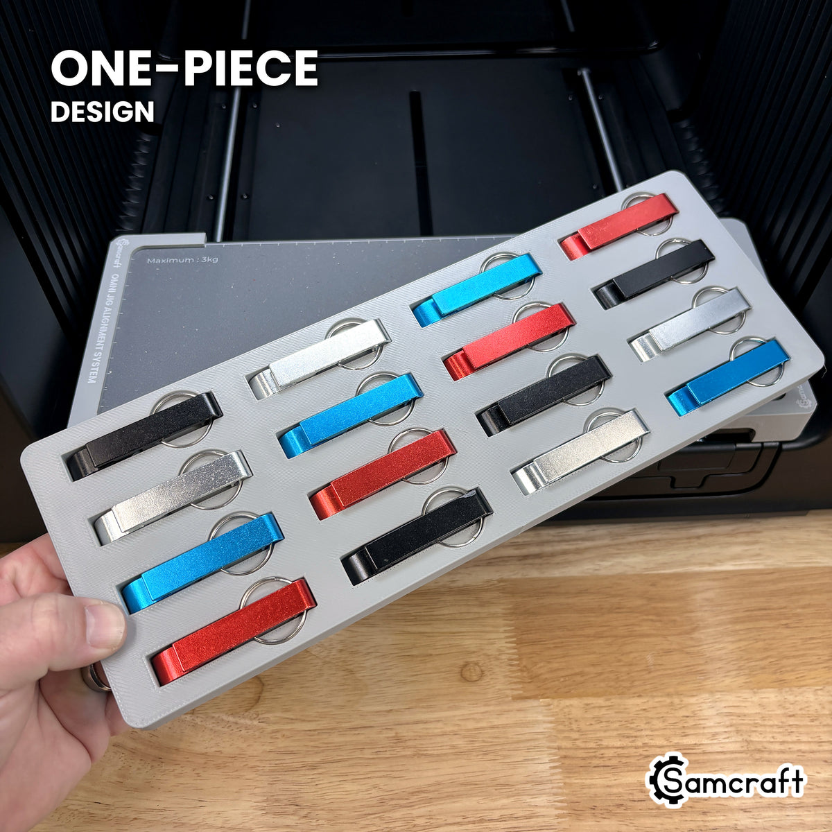 Hand holding the one-piece Samcraft keychain bottle opener jig for the xTool Omni, a single molded gray tray filled with sixteen openers.