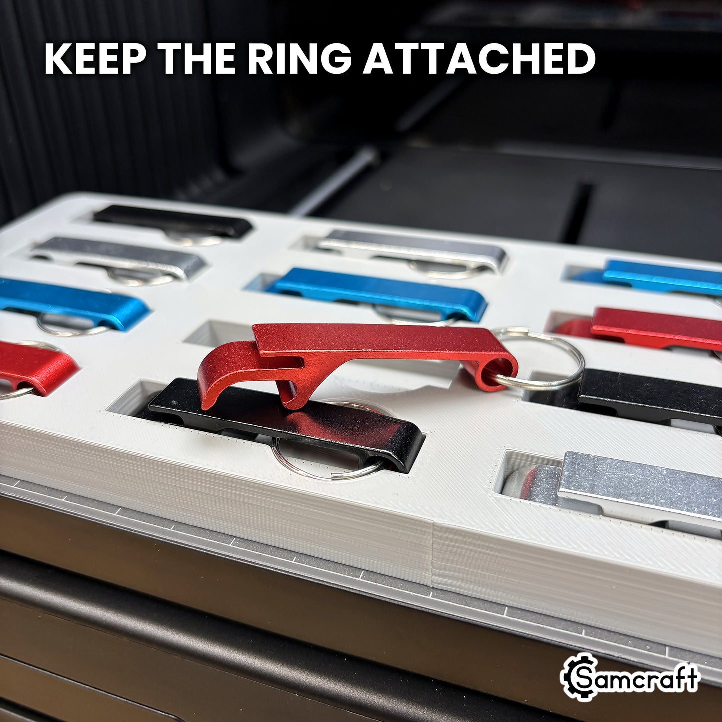 A red keychain bottle opener lifted from the Samcraft jig with its split ring still attached, showing the ring recess beneath the pocket.