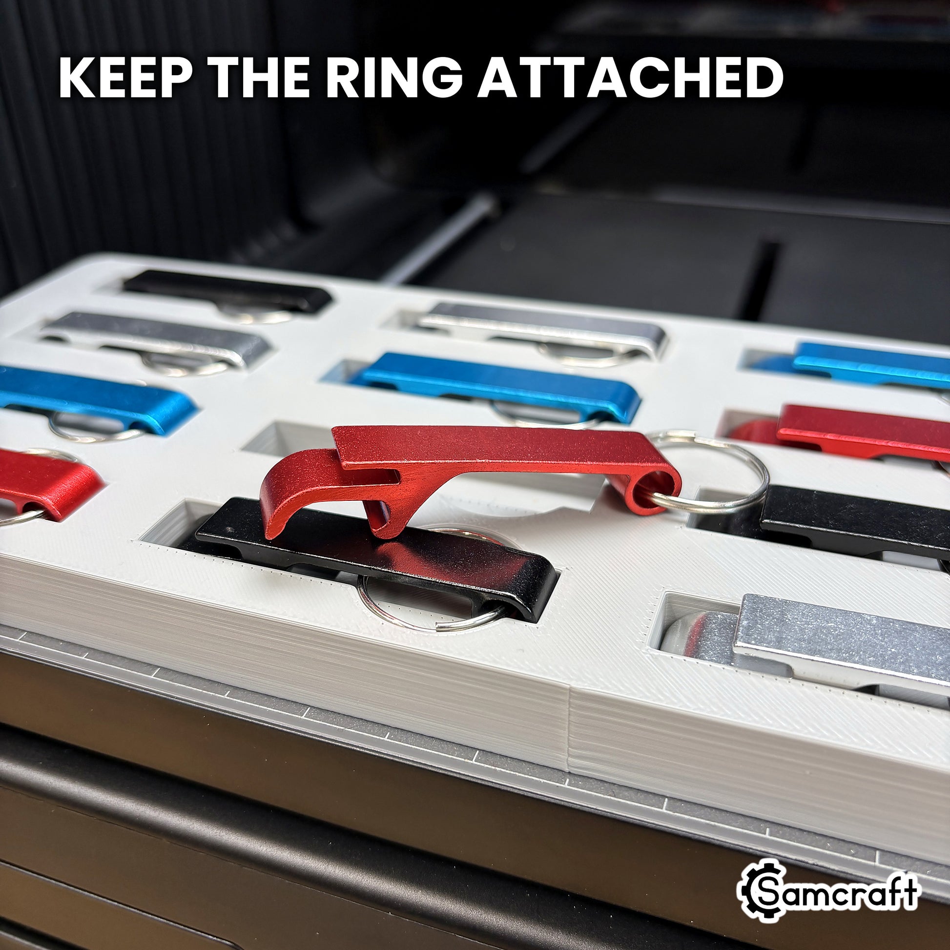 A red keychain bottle opener lifted from the Samcraft jig with its split ring still attached, showing the ring recess beneath the pocket.