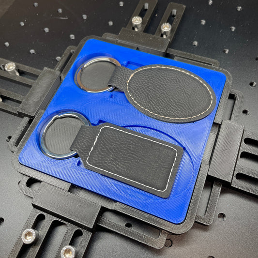 Samcraft blue leatherette keychain jig on a ComMarker laser bed, holding black oval and rectangular leatherette keychains.
