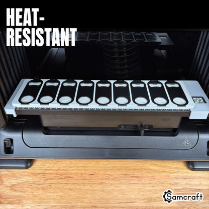 Oval Metal Bottle Opener Keychain Jig for the eufyMake E1 — front view of the gray 3D-printed tray holding nine black oval bottle openers on the printer bed with built-in alignment ruler, highlighting the heat-resistant material.