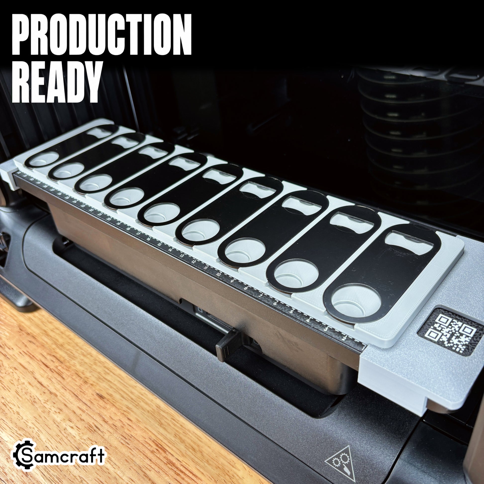 Oval Metal Bottle Opener Keychain Jig for the eufyMake E1 — angled view of the gray one-piece 3D-printed tray holding black oval bottle openers on the printer bed with built-in alignment ruler, highlighting the production-ready design.