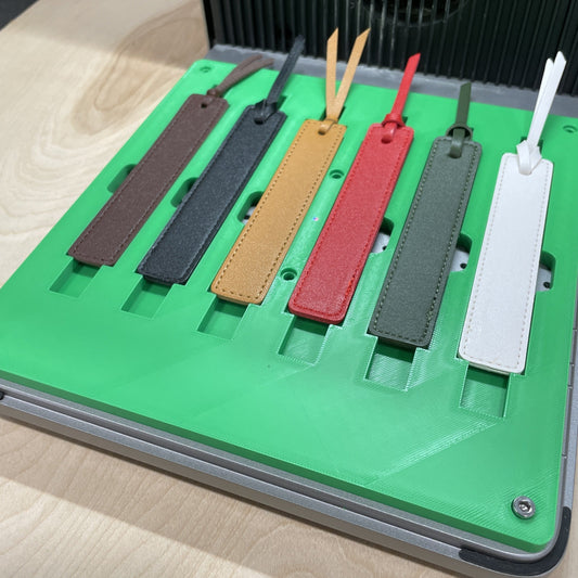 Samcraft green leather bookmark jig in an xTool F1 Ultra laser bed, holding leather bookmarks in tan, red, grey and white.