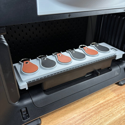 Samcraft leather key fob jig on the eufyMake E1 print bed, holding teardrop leather key fobs in tan, grey and salmon.