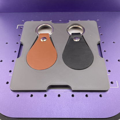 Samcraft leather key fob jig on the purple bed of a WeCreat Lumos, holding tan and black leather key fobs with split rings.