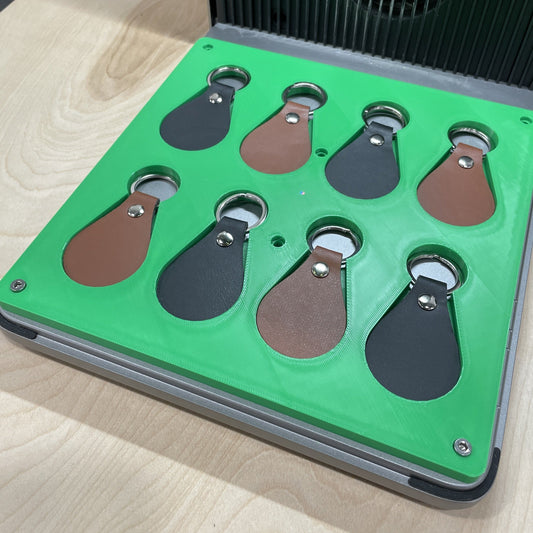 Samcraft green leather key fob jig in an xTool F1 Ultra laser bed, holding eight teardrop leather key fobs in brown and black.