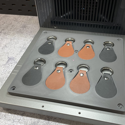 Samcraft leather key fob jig on the xTool F2 Ultra bed, holding tan leather key fobs with split rings.