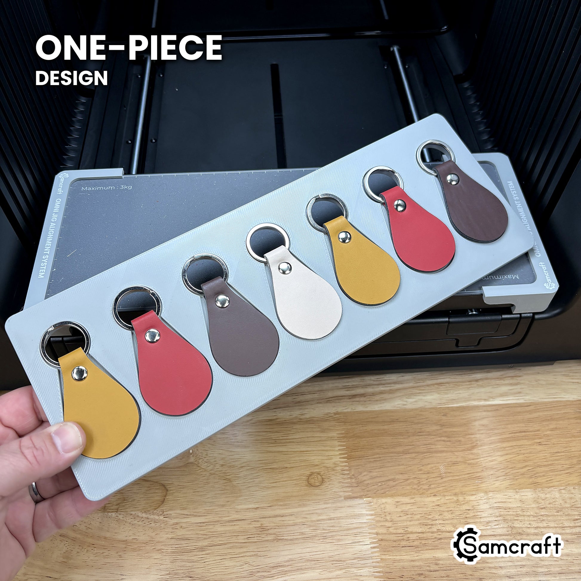 Hand holding the one-piece Samcraft leather key fob jig for the xTool Omni, a single molded gray tray holding seven leather fobs.