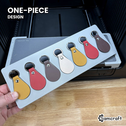 Hand holding the one-piece Samcraft leather key fob jig for the xTool Omni, a single molded gray tray holding seven leather fobs.