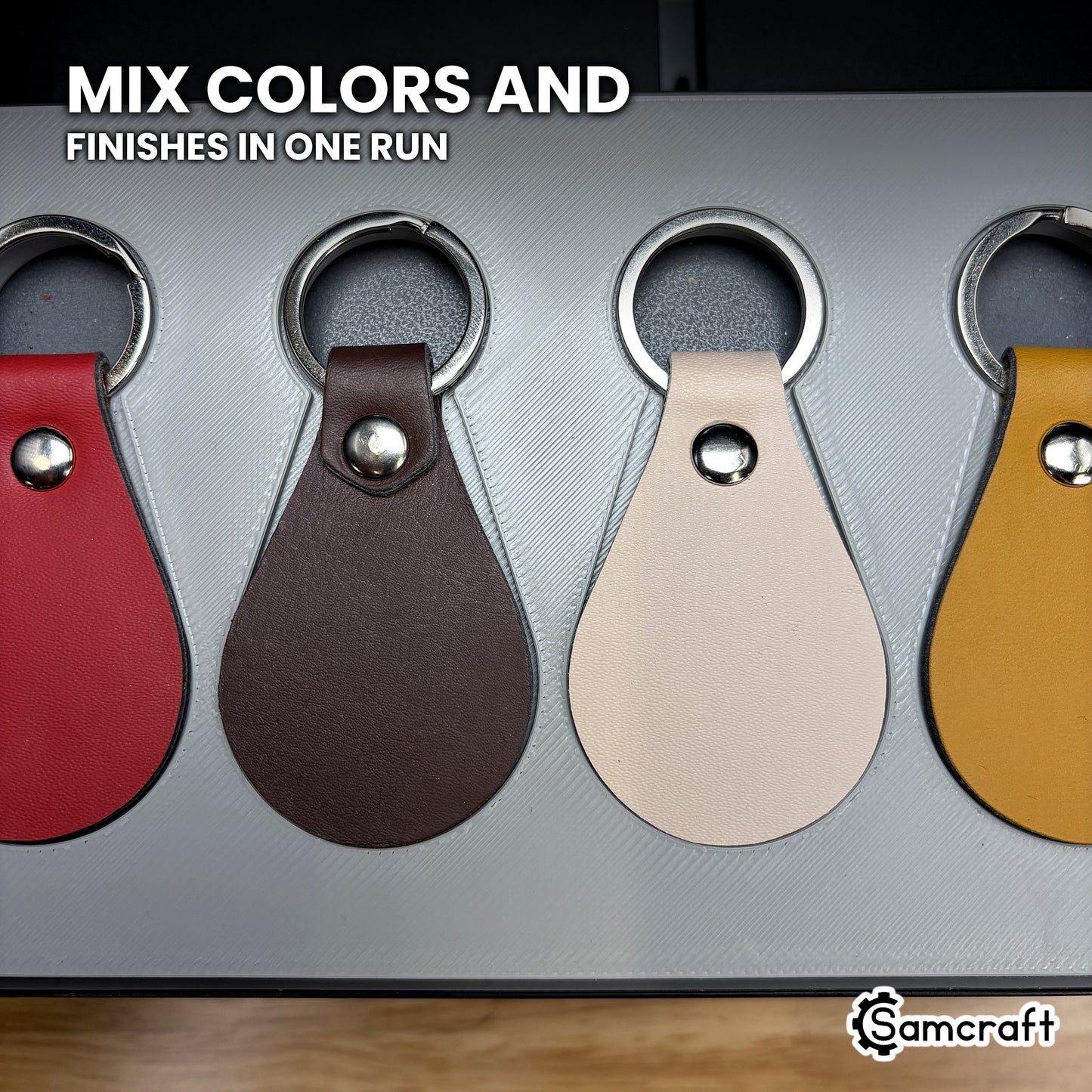 Close-up of tan, brown, cream and red leather key fobs seated side by side in the Samcraft xTool Omni jig, different colors printed in one run.