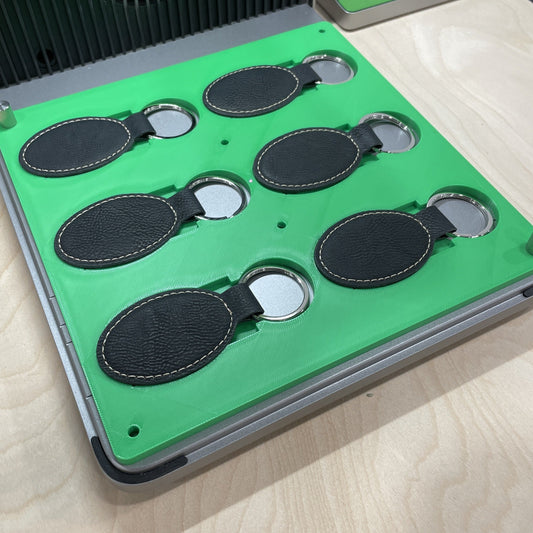 Samcraft green leatherette keychain jig in an xTool F1 Ultra laser bed, holding six oval black leatherette keychains.