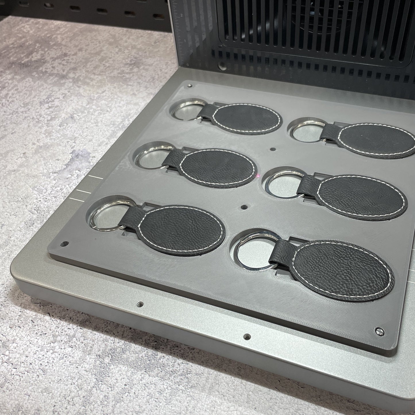 Samcraft leatherette keychain jig on the xTool F2 Ultra bed, holding oval and rectangular leatherette keychains.
