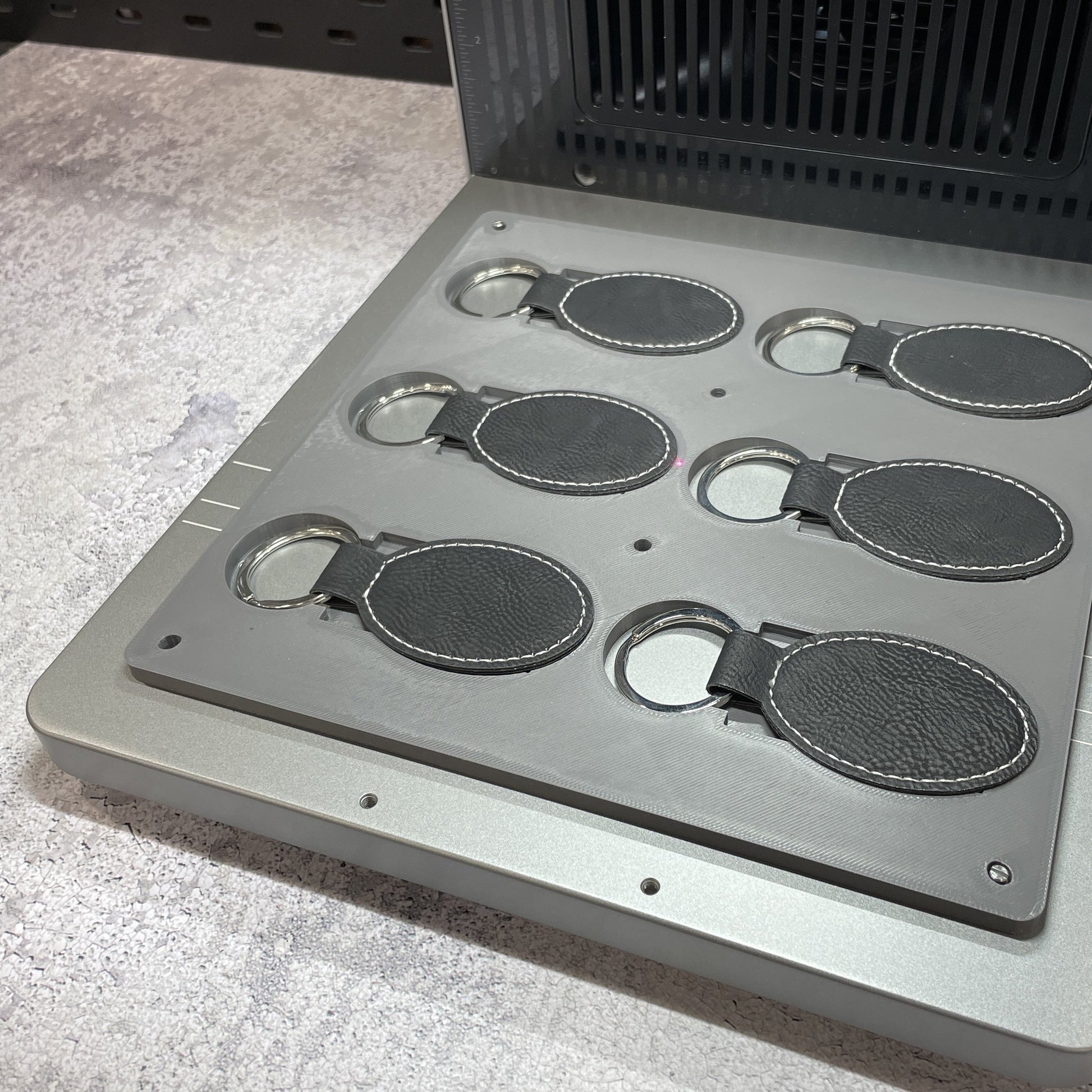 Samcraft leatherette keychain jig on the xTool F2 Ultra bed, holding oval and rectangular leatherette keychains.