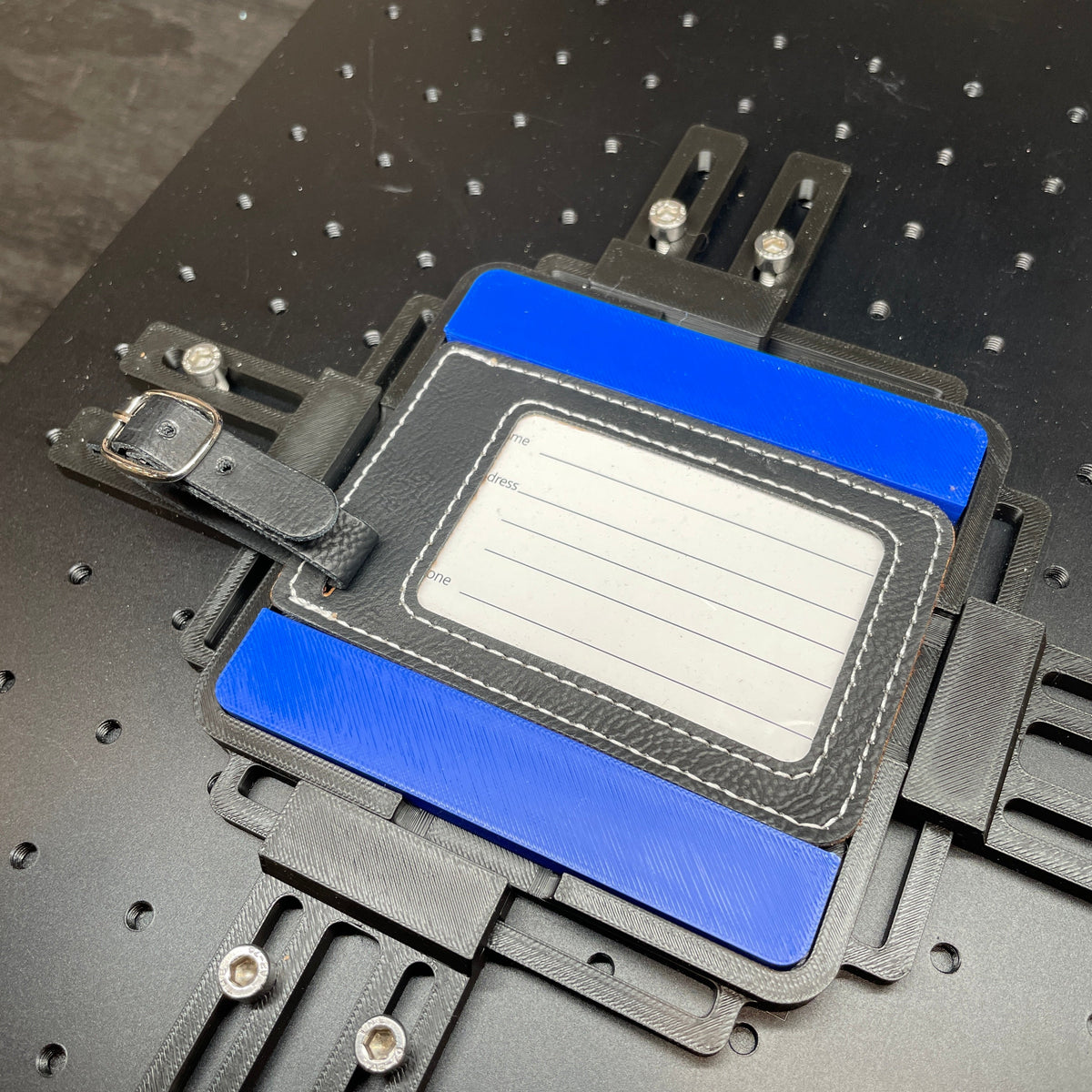 Samcraft blue leatherette luggage tag jig on a ComMarker laser bed, holding a cream leatherette luggage tag.