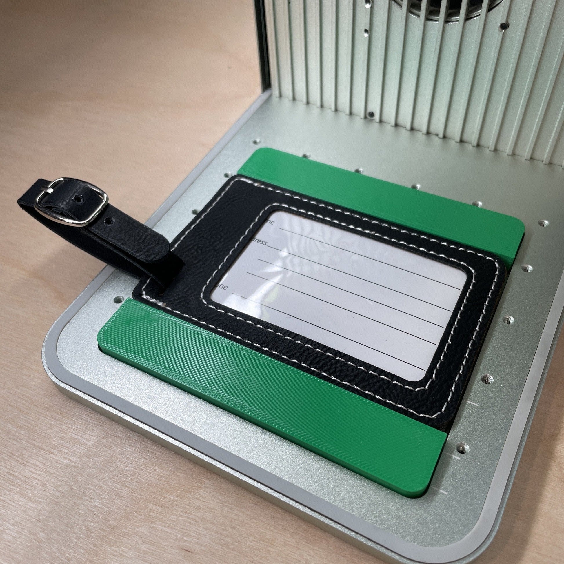 Samcraft leatherette luggage tag jig in an xTool F1 laser bed, holding a black leatherette luggage tag with its clear address window facing up.