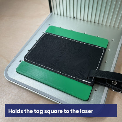 Black leatherette luggage tag held square in the Samcraft jig, strap hanging over the edge.