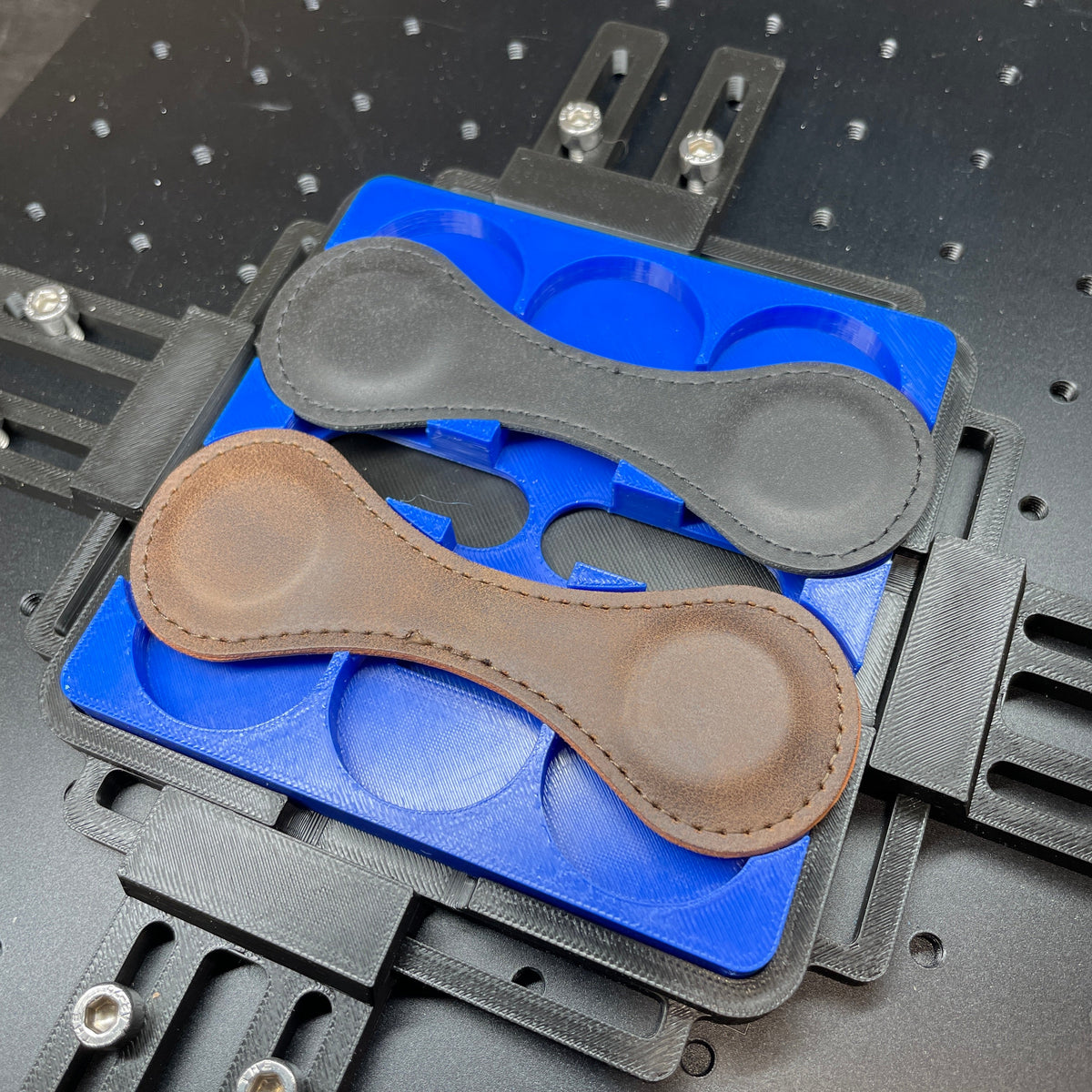 Samcraft blue magnetic bookmark jig on a ComMarker laser bed, holding grey and tan leather bookmarks.