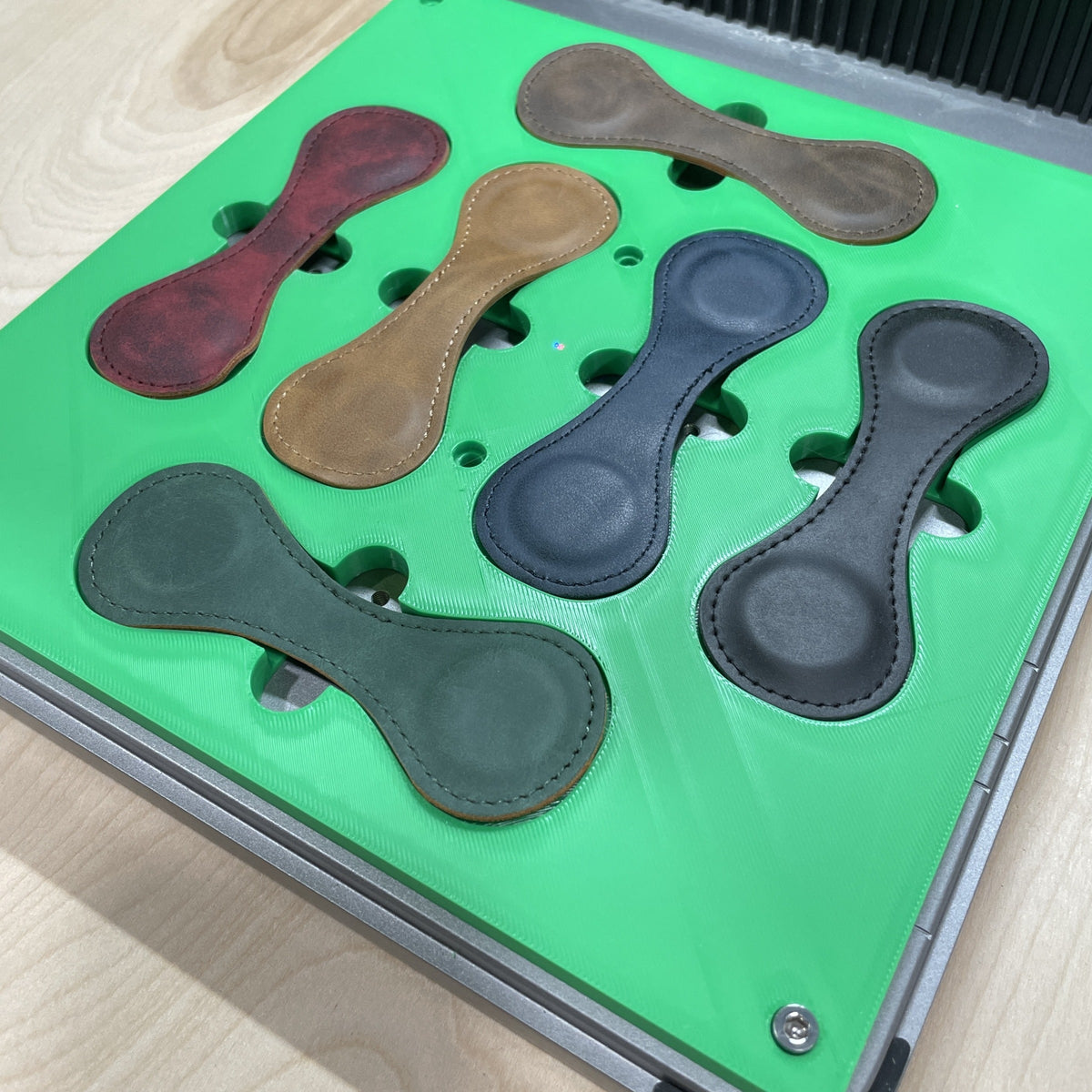 Samcraft green magnetic bookmark jig in an xTool F1 Ultra laser bed, holding wrap-style leather bookmarks in red, tan, grey and green.