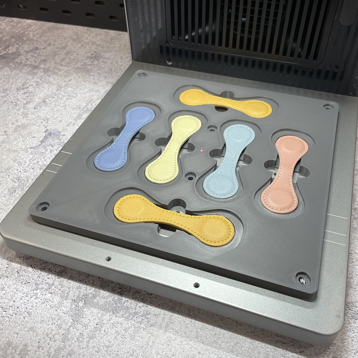 Samcraft magnetic bookmark jig on the xTool F2 Ultra bed, holding wrap-style leather bookmarks in pastel colours.