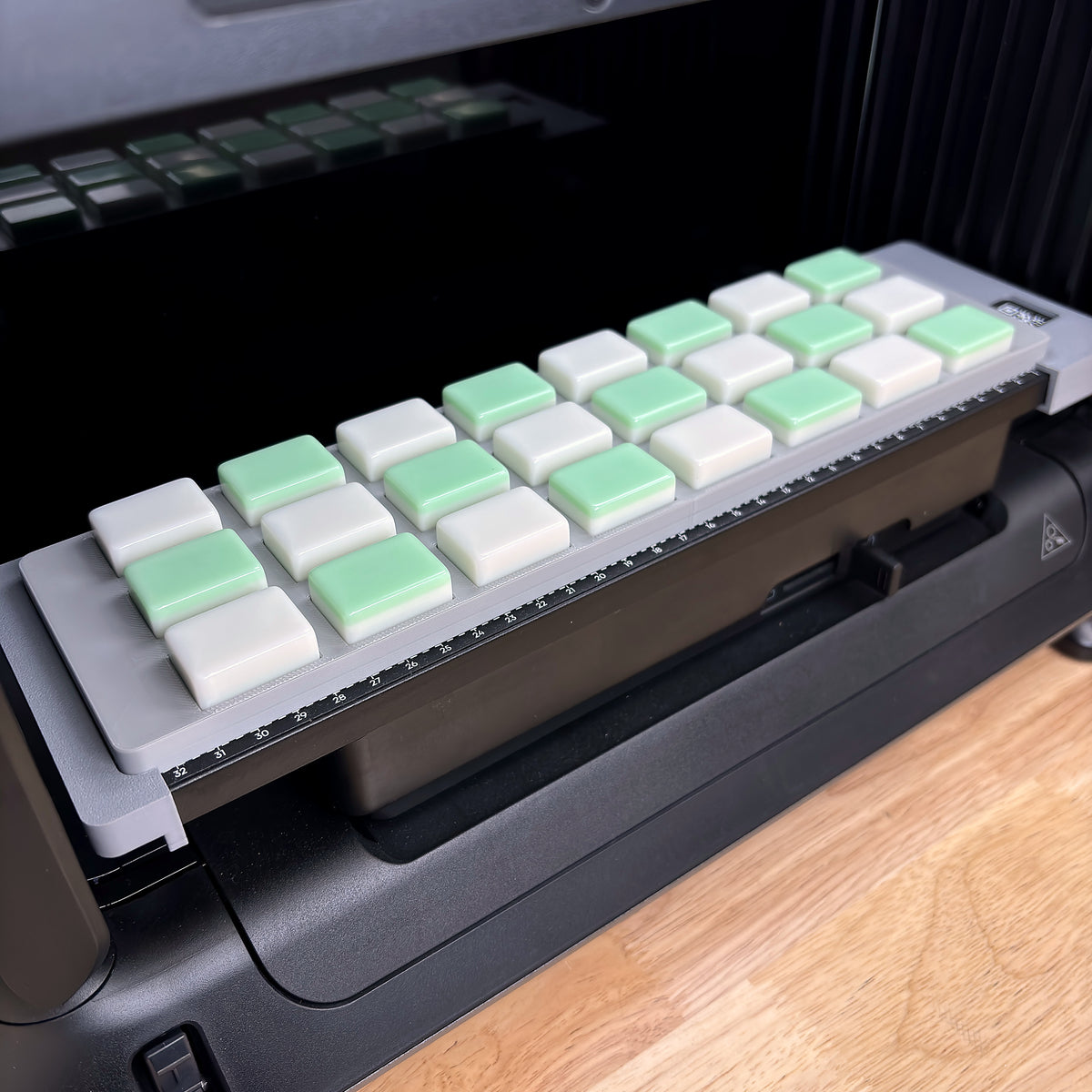 Samcraft mahjong tile jig on the bed of a eufyMake E1 UV printer, loaded with 24 blank tiles in three rows of eight, white and green tiles alternating.