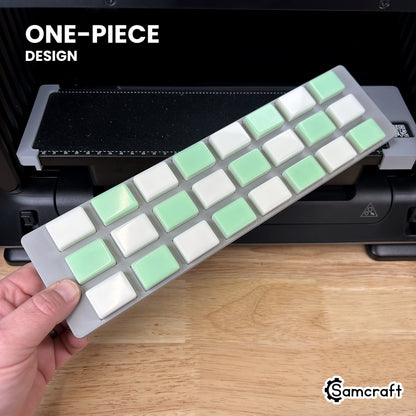Hand holding the one-piece Samcraft mahjong tile jig for the eufyMake E1, loaded with 24 tiles, in front of the printer bed.
